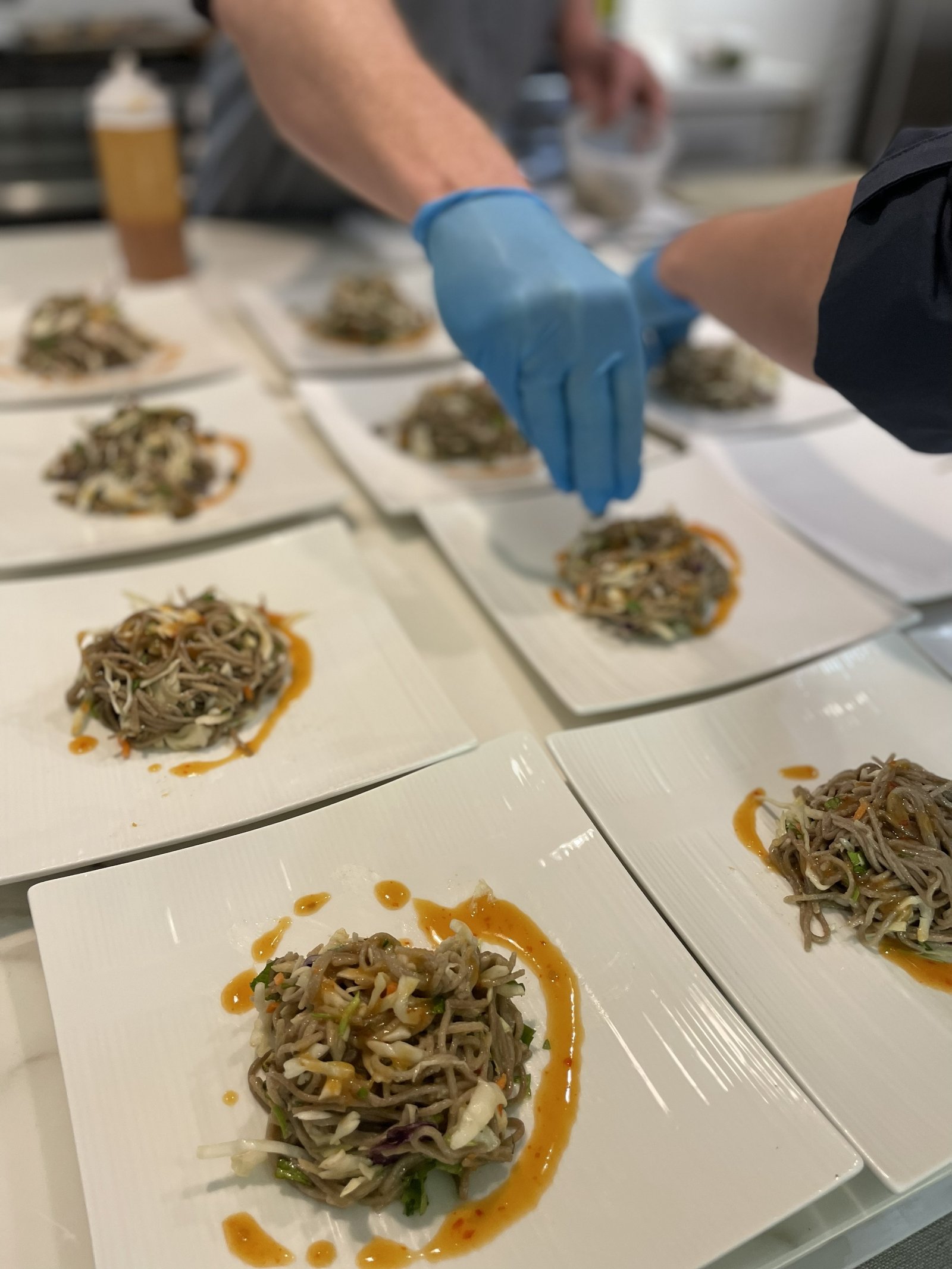 Gloved hands adding finishing touches to a row of plated dishes